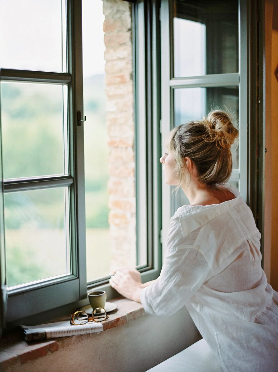 Woman gazing out a window beside a book